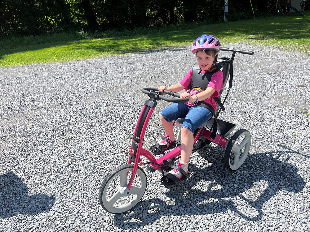A young girl smiling on an adaptive tricycle